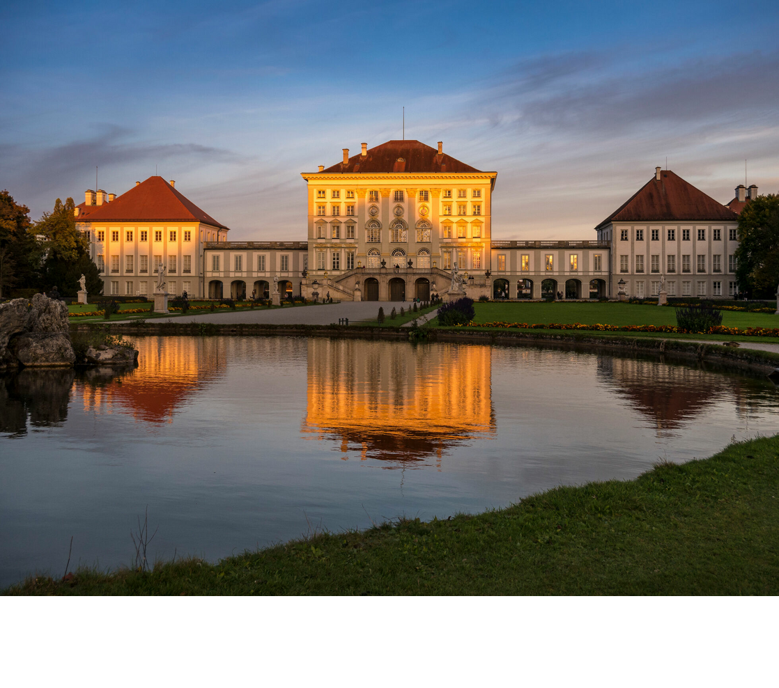 Schloss Nymphenburg in München Historisches Schloss mit roten Dächern, umgeben von gepflegtem Garten und Teich, spiegelt sich im Wasser bei Sonnenuntergang.