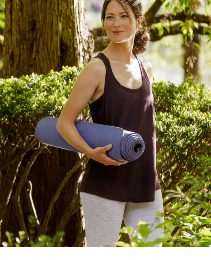 Woman with yoga mat next to a tree