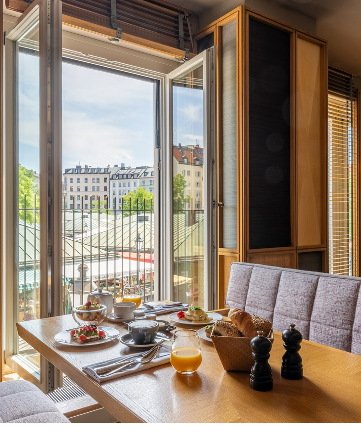 breakfast at the Grillroom LOUIS | LOUIS Hotel Munich Breakfast table at the LOUIS Hotel with a view of Munich's rooftops through an open window.