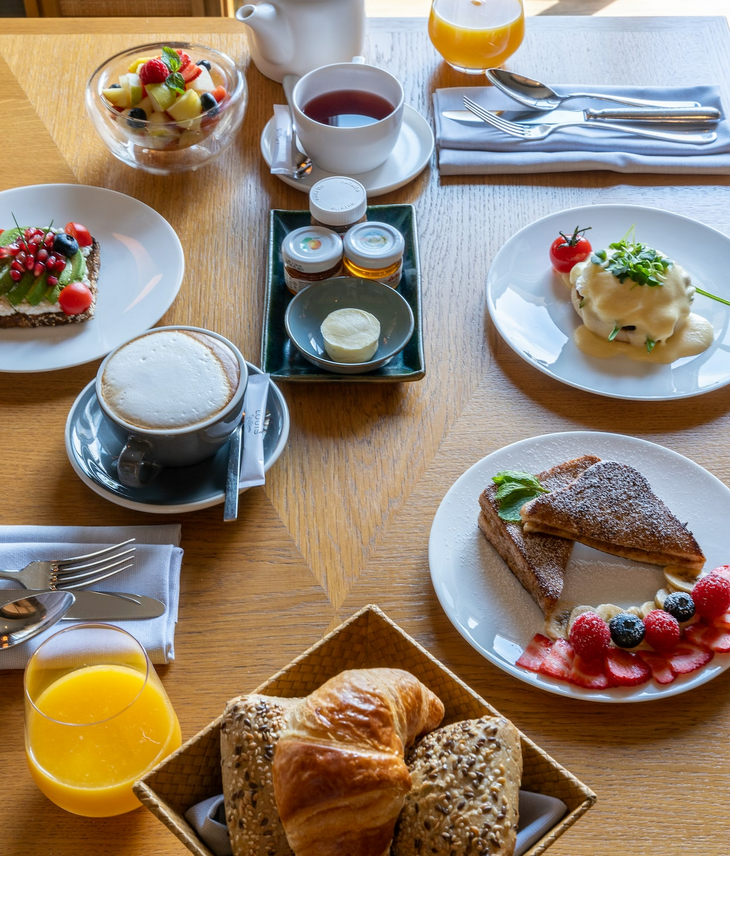 Frühstücken im LOUIS Hotel München am Viktualienmarkt Frühstückstisch im LOUIS Hotel München mit Gebäck, Obst, Kaffee, Tee und Saft, elegant angerichtet auf Holztisch.