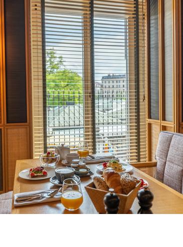 Gemütliche Frühstücksecke im LOUIS Hotel mit gedecktem Tisch, Blick durch Fensterläden auf Stadtlandschaft.
