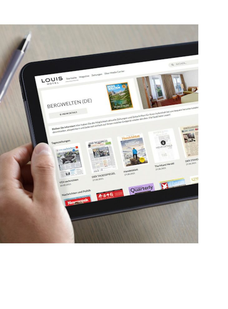 Person holds a tablet with a hotel website, next to it a cup of coffee on a table.
