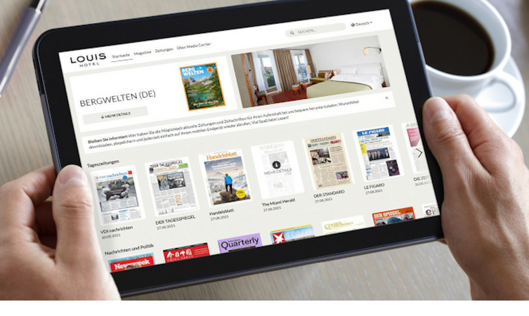 Person holds a tablet with a hotel website, next to it a cup of coffee on a table.