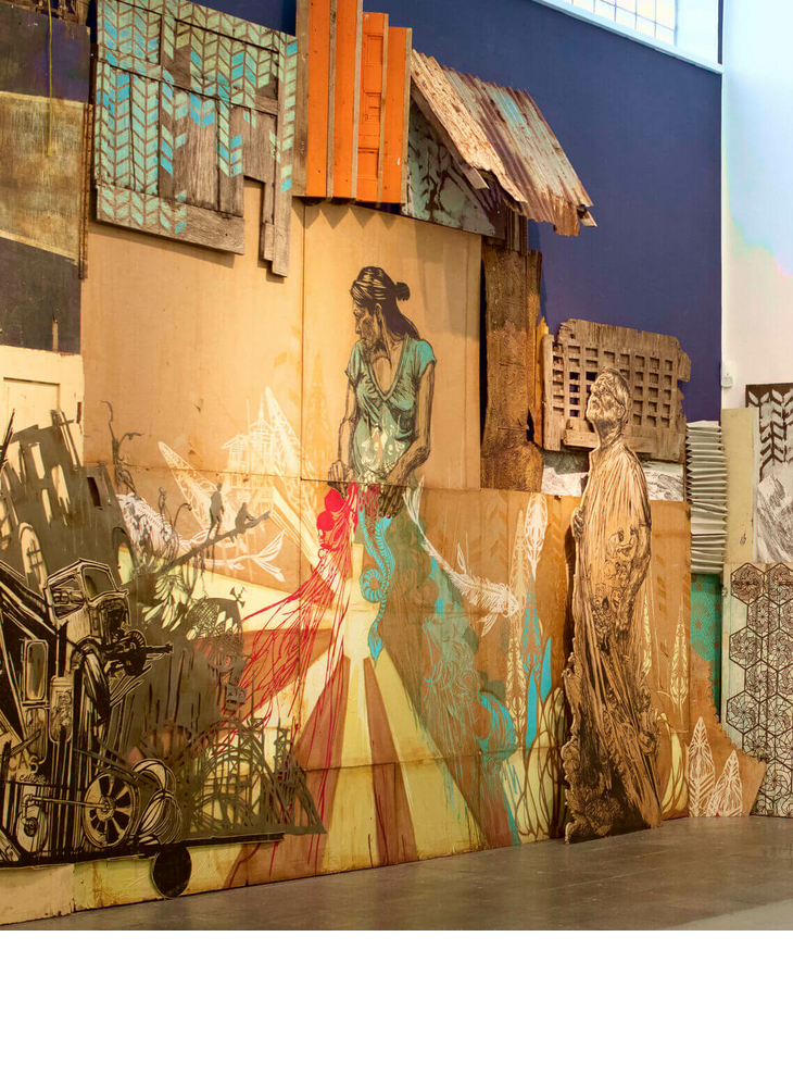 Wandkunstinstallation aus bemaltem Holz und Pappe mit Figuren und Mustern in einem modernen Ausstellungsraum.