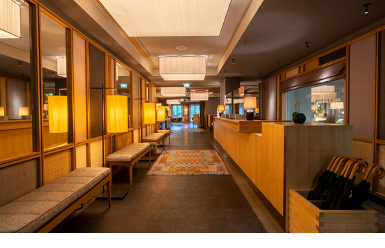 Lobby mit Rezeption im LOUIS Hotel München Elegante Hotel-Lobby mit Holzwänden, warmem Licht, Sitzbänken und Teppich im LOUIS Hotel München.
