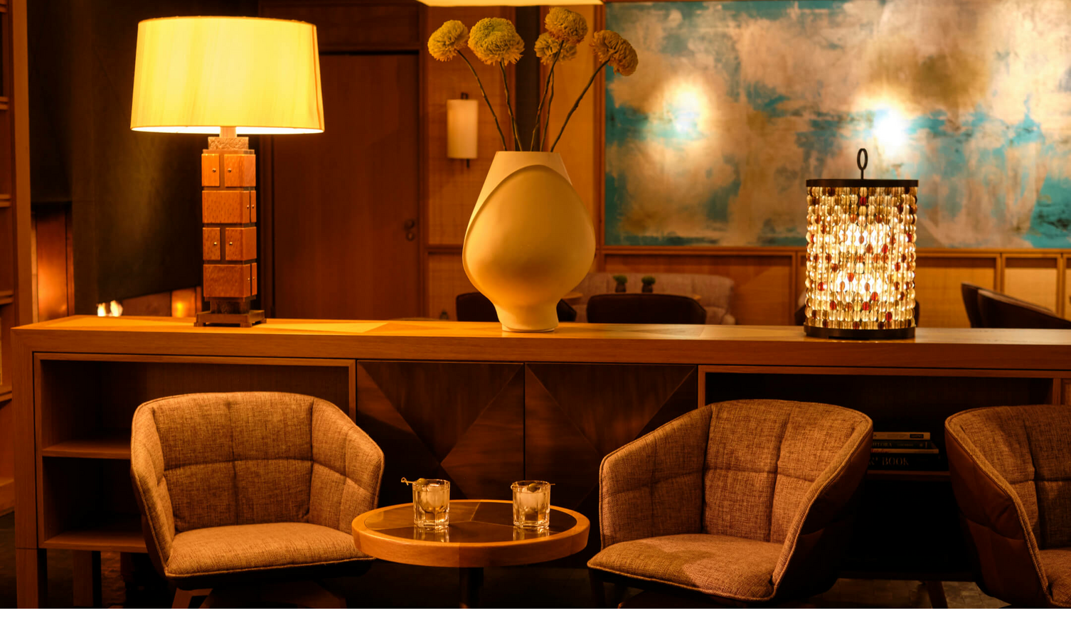 Cozy lounge in the LOUIS Hotel Munich with armchairs, table, lamp and stylish decoration in warm light.