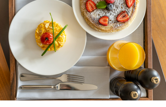 Frühstückstablett mit Rührei, Tomate, Pfannkuchen mit Beeren, Orangensaft und Gewürzmühlen im LOUIS Hotel München.