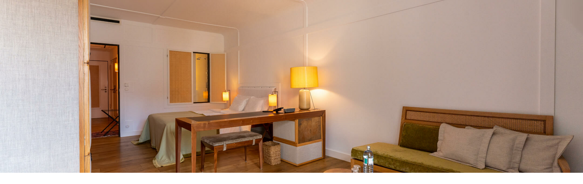 Bright hotel room with wooden floor, bed, desk, sofa, carpet and table lamps at the LOUIS Hotel Munich.