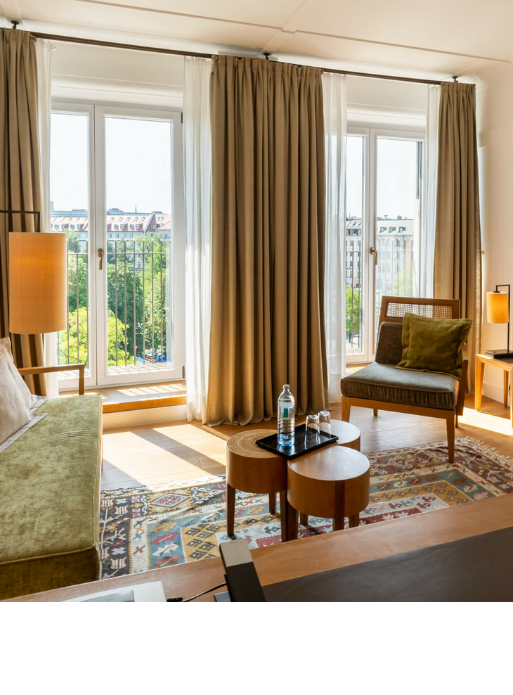 LOUIS Hotel Munich | Market View Deluxe Room Bright hotel room with modern furniture, large windows and a view of the city at the LOUIS Hotel Munich.