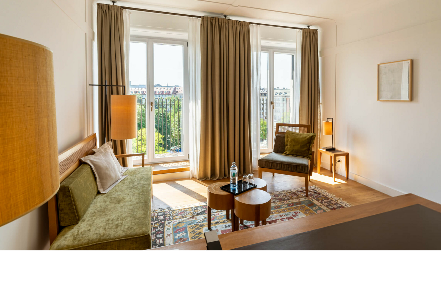 Bright hotel room with modern furniture, large windows and a view of the city at the LOUIS Hotel Munich.