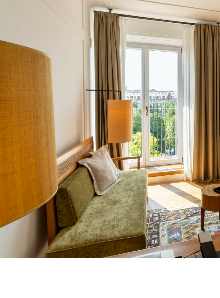 Bright hotel room with modern furniture, large windows and a view of the city at the LOUIS Hotel Munich.