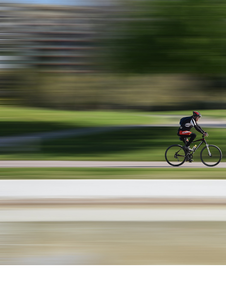 Race - Radrennfahrer Radfahrer mit rotem Helm fährt schnell auf einem Radweg durch einen grünen Park.