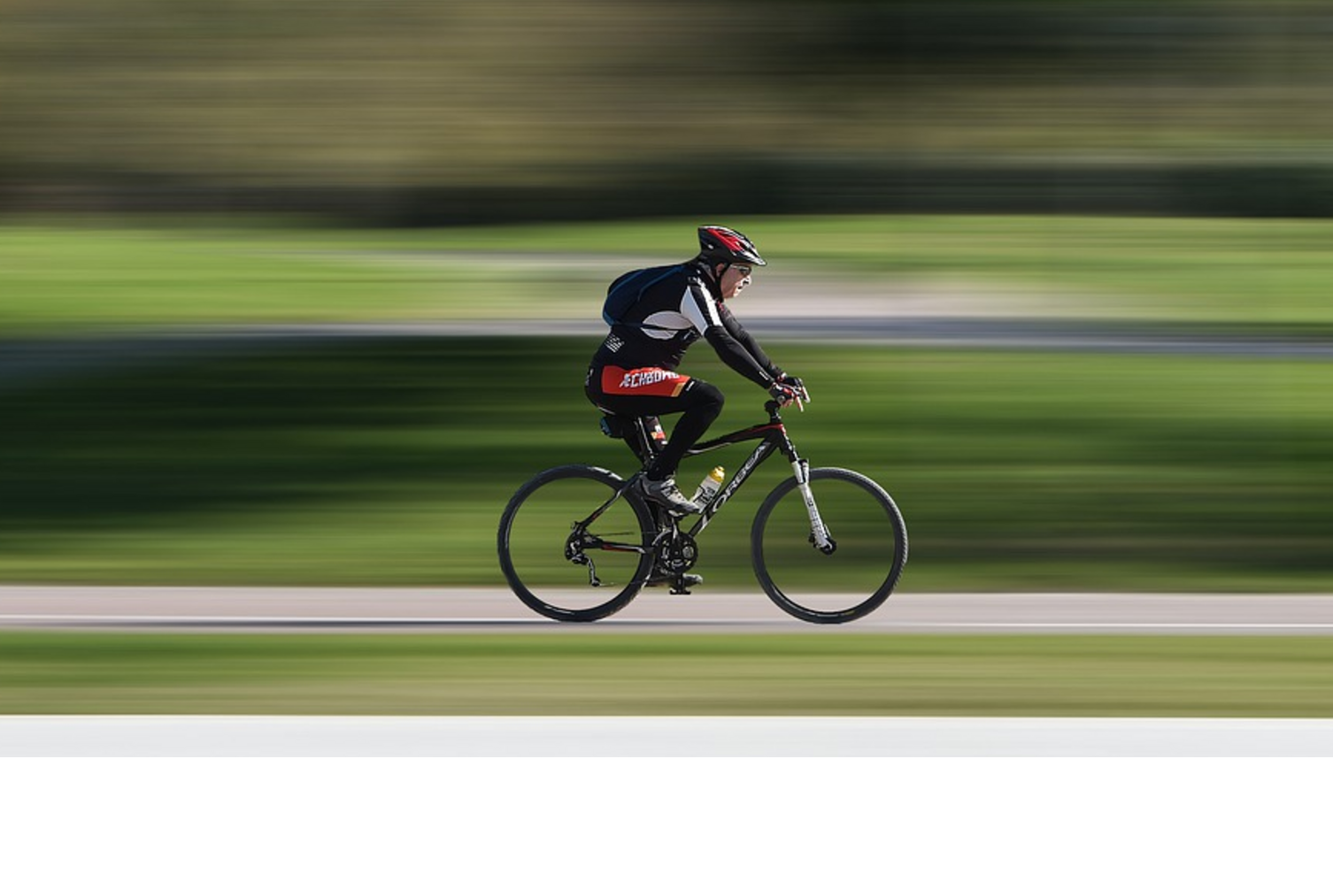Race - Radrennfahrer Radfahrer mit rotem Helm fährt schnell auf einem Radweg durch einen grünen Park.