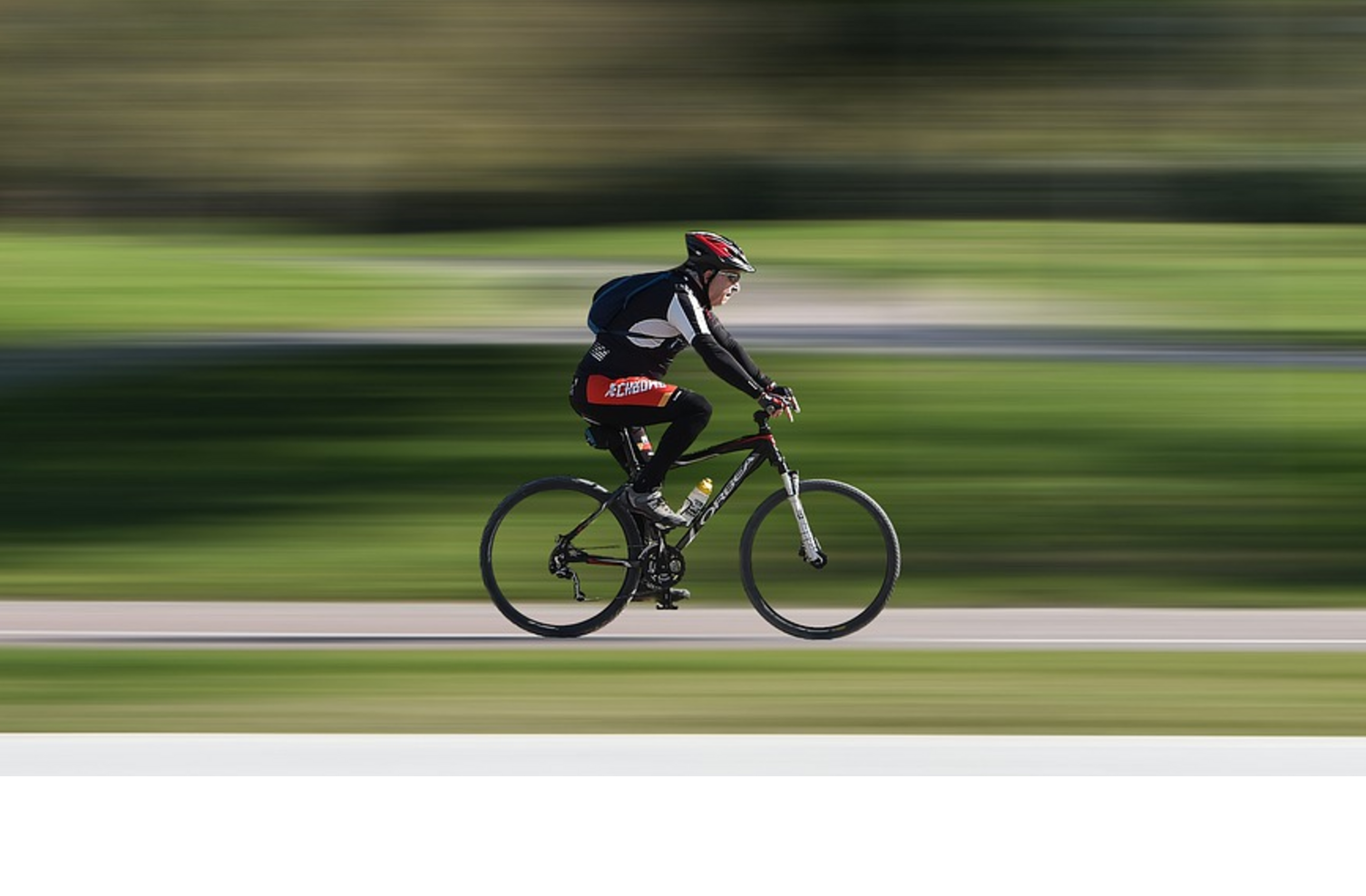 Cyclist wearing a red helmet riding fast on a cycle path through a green park.