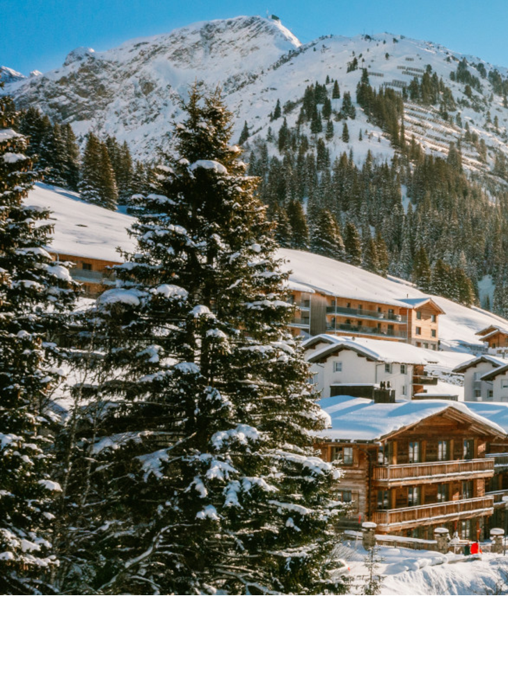 Snowy alpine landscape with sun above Hotel Severin*s in Lech, surrounded by mountains and trees.
