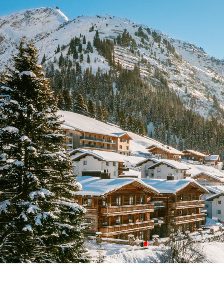 Verschneite Alpenlandschaft mit Sonne über Hotel Severin*s in Lech, umgeben von Bergen und Bäumen.