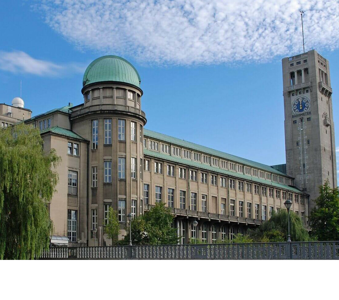 Historisches Gebäude mit grünem Kuppeldach und Turmuhr vor blauem Himmel.