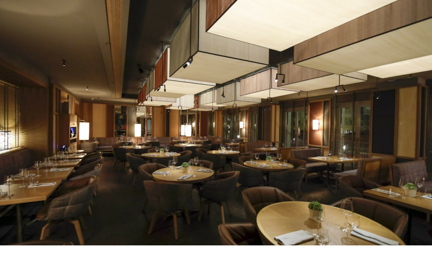 The LOUIS Grillroom am Viktualienmarkt in München Elegantes Hotelrestaurant mit runden Holztischen, bequemen Stühlen und stimmungsvoller Beleuchtung.