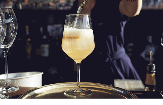 Aperitif auf der The LOUIS Roof Terrace Ein prickelndes Getränk wird in ein Weinglas auf einem Tablett im LOUIS Hotel München eingeschenkt.