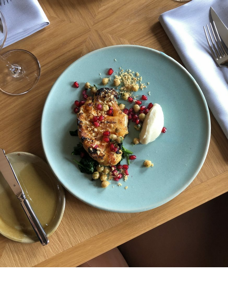 The LOUIS Grillroom l Blumenkohlsteak Elegantes Gericht mit gegrilltem Gemüse, Kichererbsen, Granatapfelkernen und Creme auf blauem Teller im LOUIS Hotel.