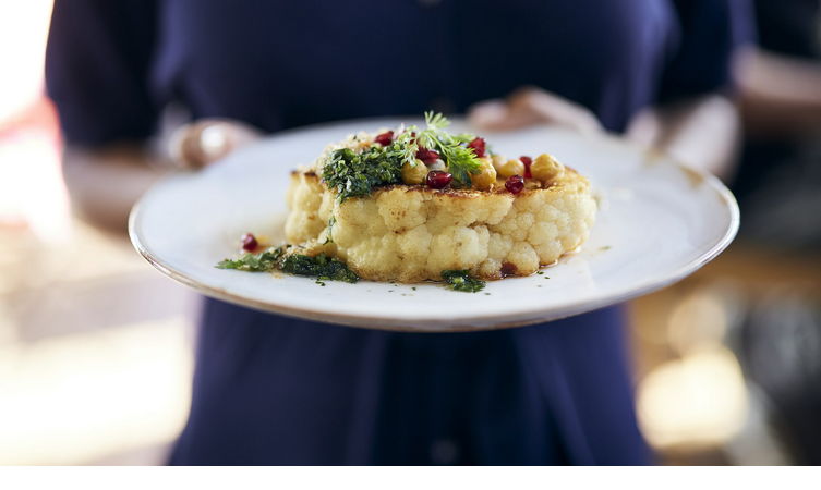 A plate of artfully arranged cauliflower, garnished with herbs and pomegranate seeds.