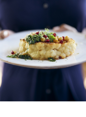 A plate of artfully arranged cauliflower, garnished with herbs and pomegranate seeds.