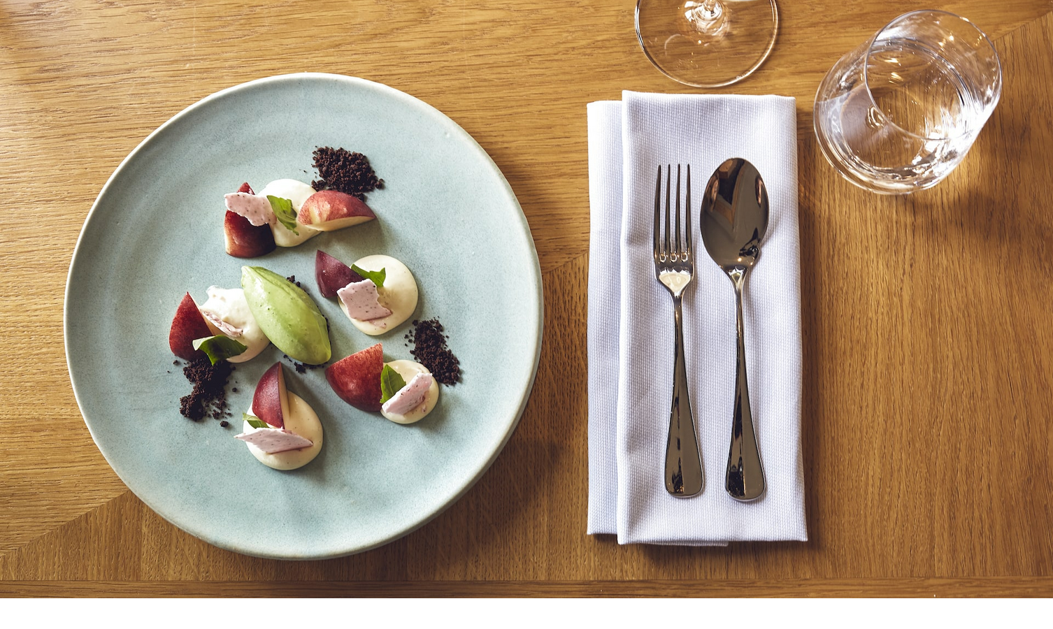 Elegant dessert on a blue plate with cutlery and glasses on a wooden table in the LOUIS Hotel Munich.