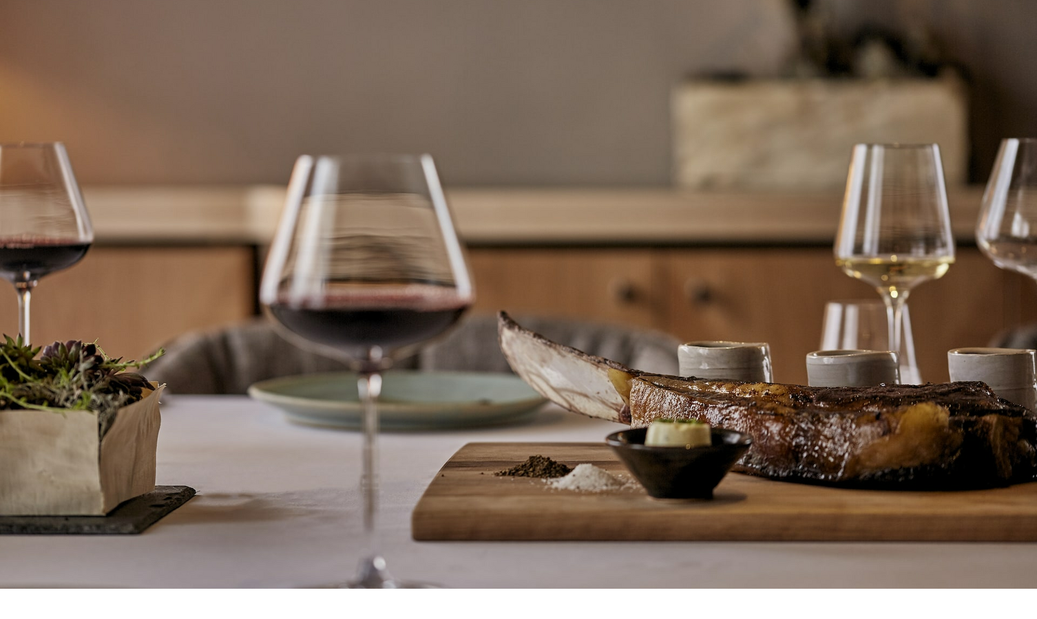 Elegant restaurant setting with wine glasses and a wooden board with grilled meat and spices at the LOUIS Hotel Munich.