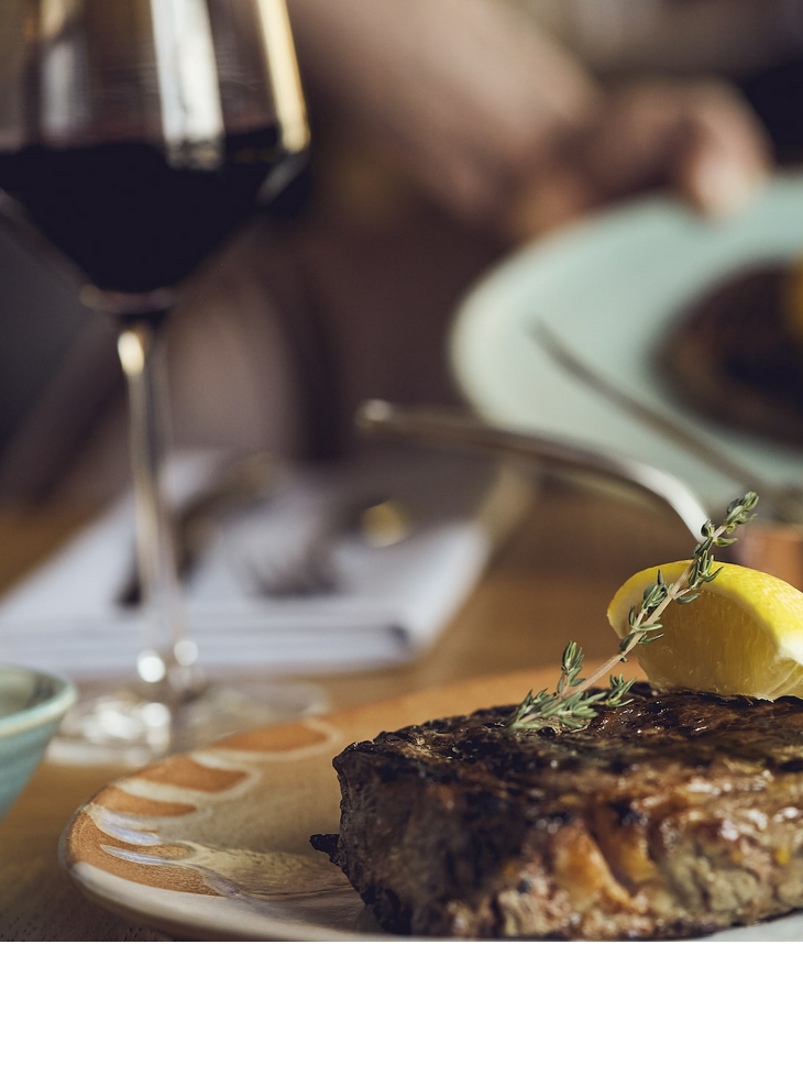 A juicy steak with a slice of lemon and thyme, served on a plate at the LOUIS Hotel Munich.