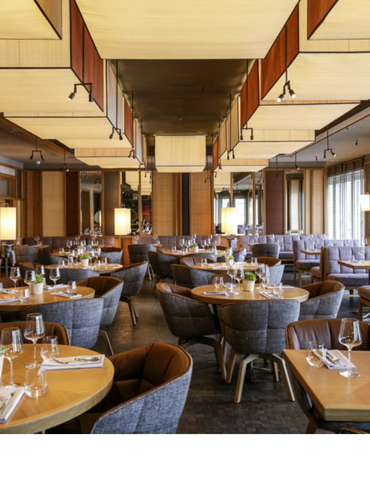 Modern restaurant in the LOUIS Hotel Munich with stylish wooden tables, set with glasses and cutlery, cozy seating.