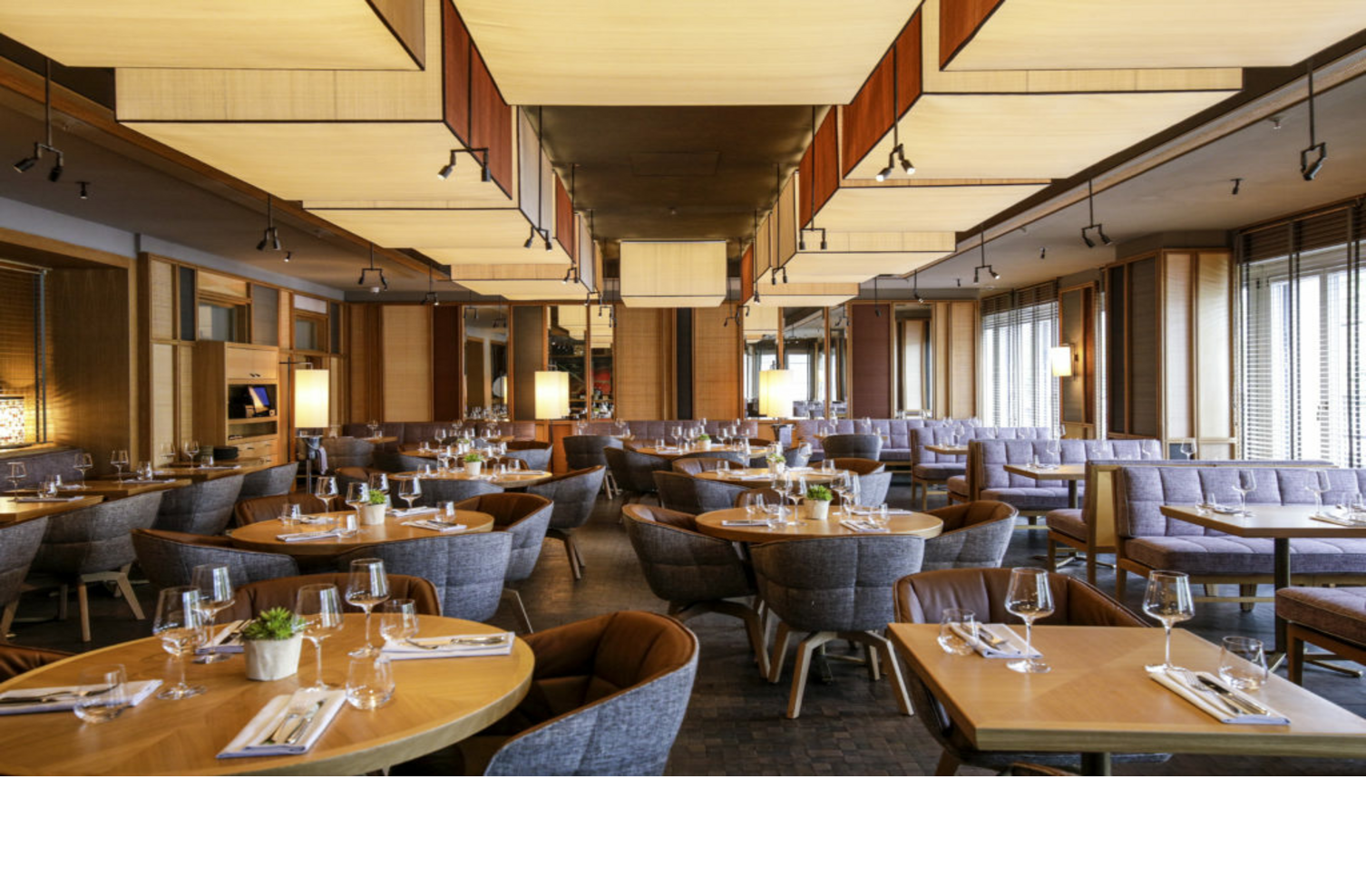 Modern restaurant in the LOUIS Hotel Munich with stylish wooden tables, set with glasses and cutlery, cozy seating.