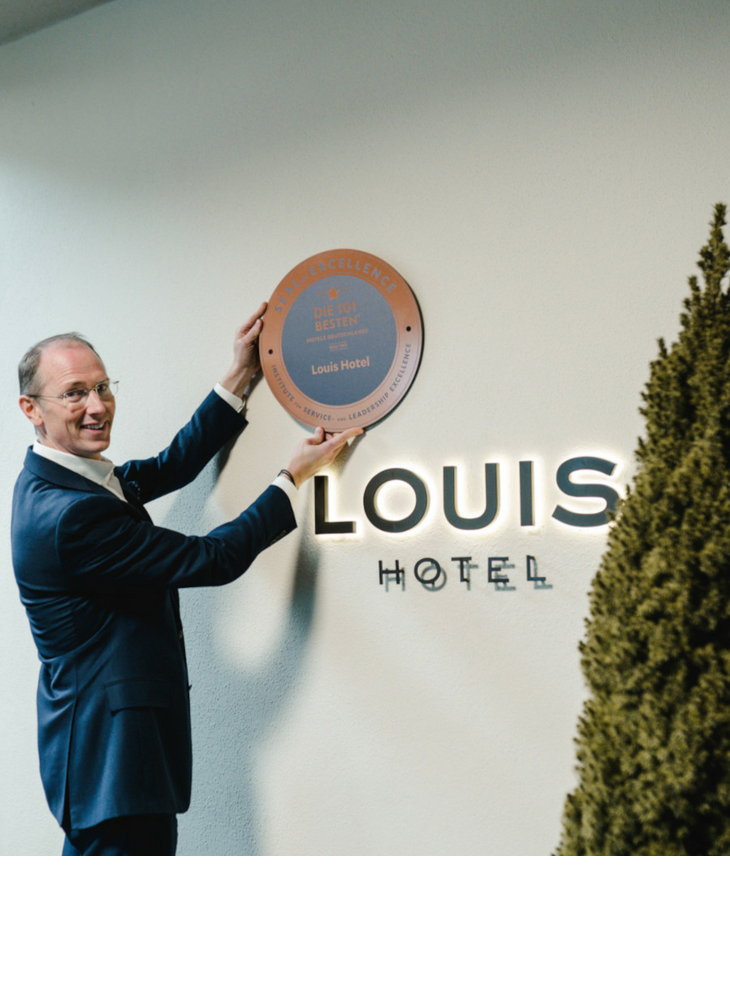 Direktor, Mike Fuchs, hängt das 101-Beste Hotels Zertifikat am LOUIS Hotel in München auf