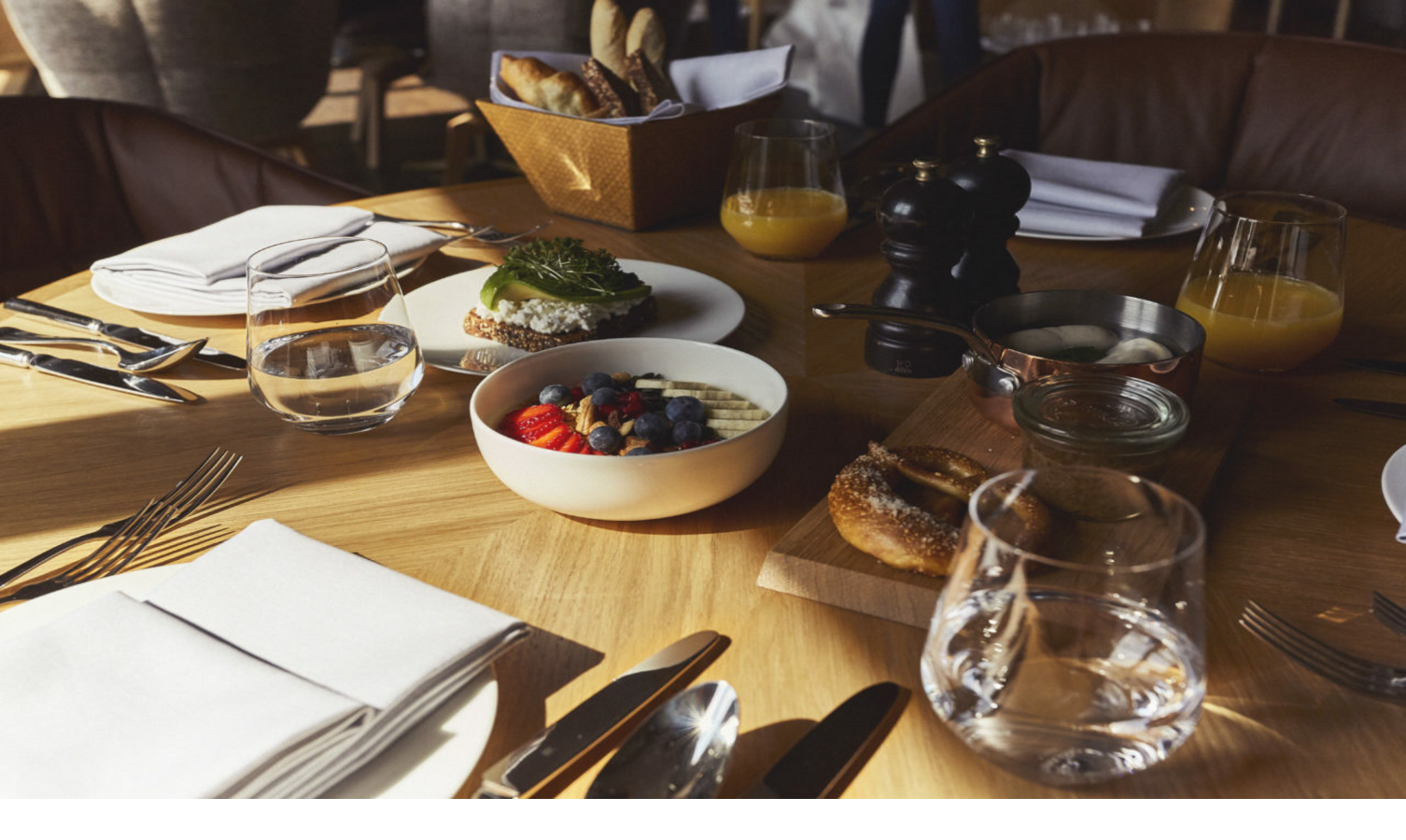 Breakfast table at the LOUIS Hotel Munich with fruit bowl, bread, juice and cutlery on a wooden table.