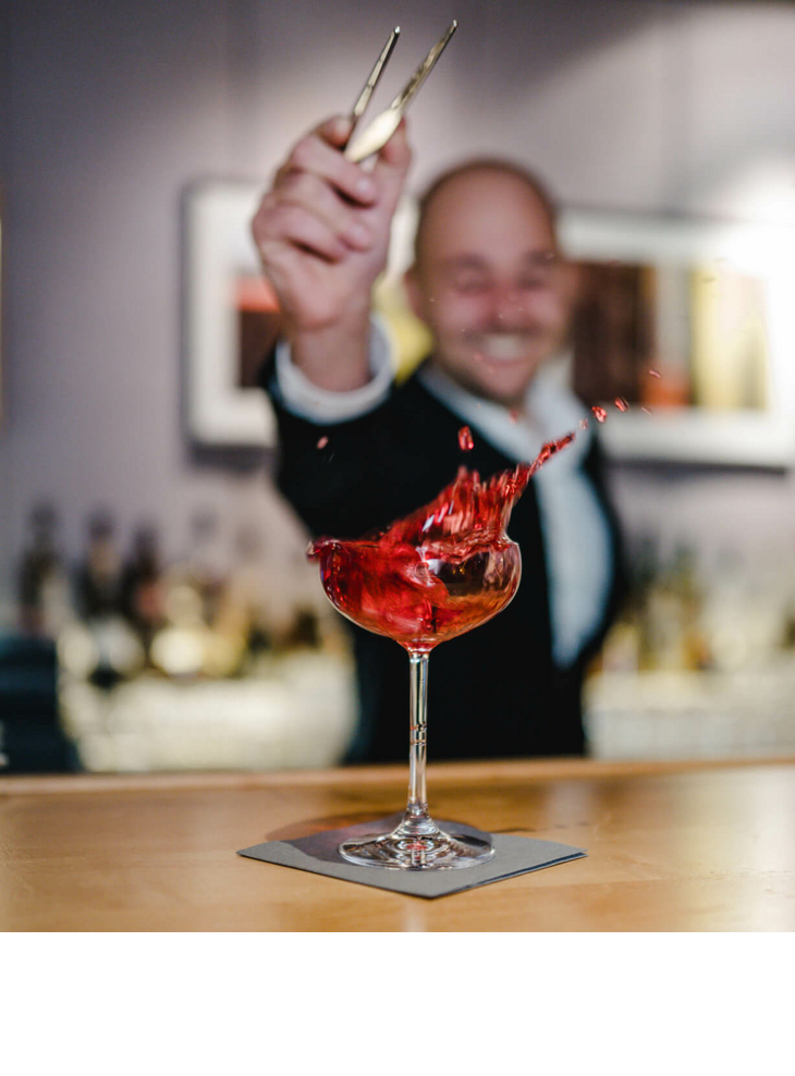 Ein Barkeeper im LOUIS Hotel München mixt einen spritzenden roten Cocktail.