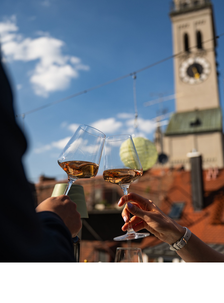 Two people are enjoying a glass of wine on the roof terrace, with St Peter’s Church in the background.