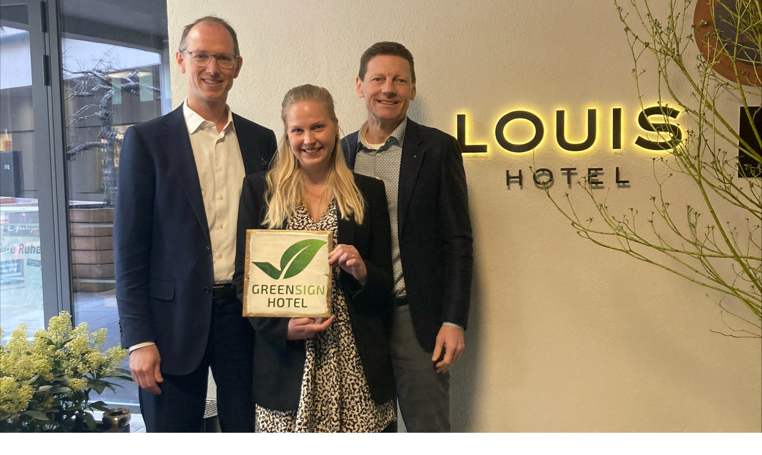 Three people in front of the LOUIS Hotel logo hold a Greensign certificate, which recognizes sustainability.