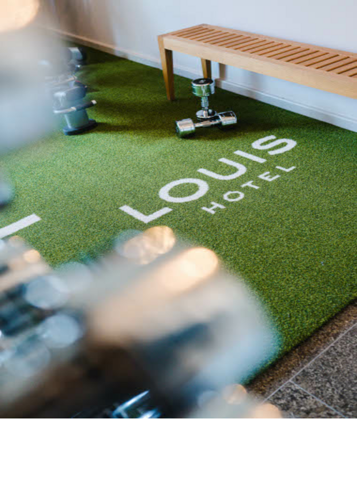 Der grüne Teppich im Fitnessbereich des Hotels mit weißer Aufschrift: „LOUIS Hotel“